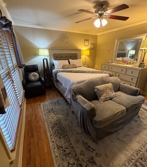 A bedroom with a bed, two chairs, a ceiling fan, a dresser, and a mirror. - FIFA READY! Spacious 8-bedroom Retreat in Stone Mountain (stone mountain)