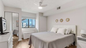 A bedroom with a bed, a desk, a chair, a TV, and a window. - Jamaica Bay 308B (Ocean City)