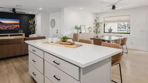 Een moderne keuken met een centraal eiland, een eethoek met stoelen, een aan de muur bevestigde televisie en een raam met uitzicht.