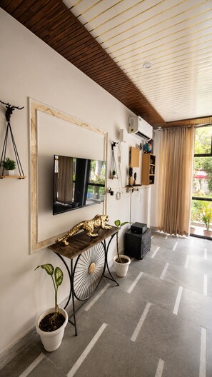 Una sala moderna con un televisor de pantalla plana, una mesa consola de madera, plantas en macetas y un techo con vigas de madera.