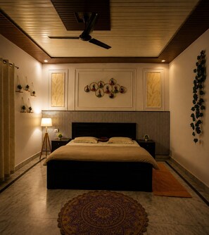 Un dormitorio con una cama, ventilador de techo, una obra de arte en la pared, mesita de noche y lámpara de pie.