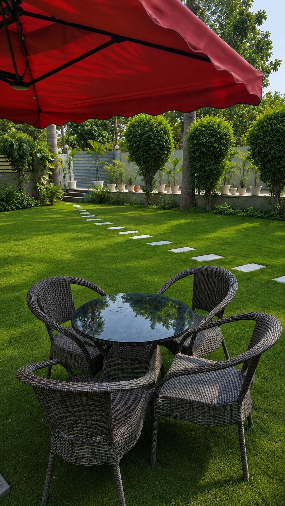 A patio area with a round table and wicker chairs, surrounded by a well-manicured lawn and potted plants.