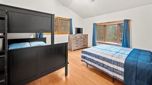 Ein Schlafzimmer mit Etagenbett, einem Einzelbett, einer Holzkommode, einem Fernseher und großen, mit Vorhängen versehenen Fenstern.
