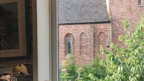 A window with a view of a brick building, a potted plant, and a lamp on a windowsill. - B&B De Zwerver (Oldehove)