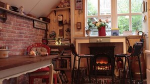 A cozy room with a brick wall, a fireplace, and a window with flowers. - B&B De Zwerver (Oldehove)