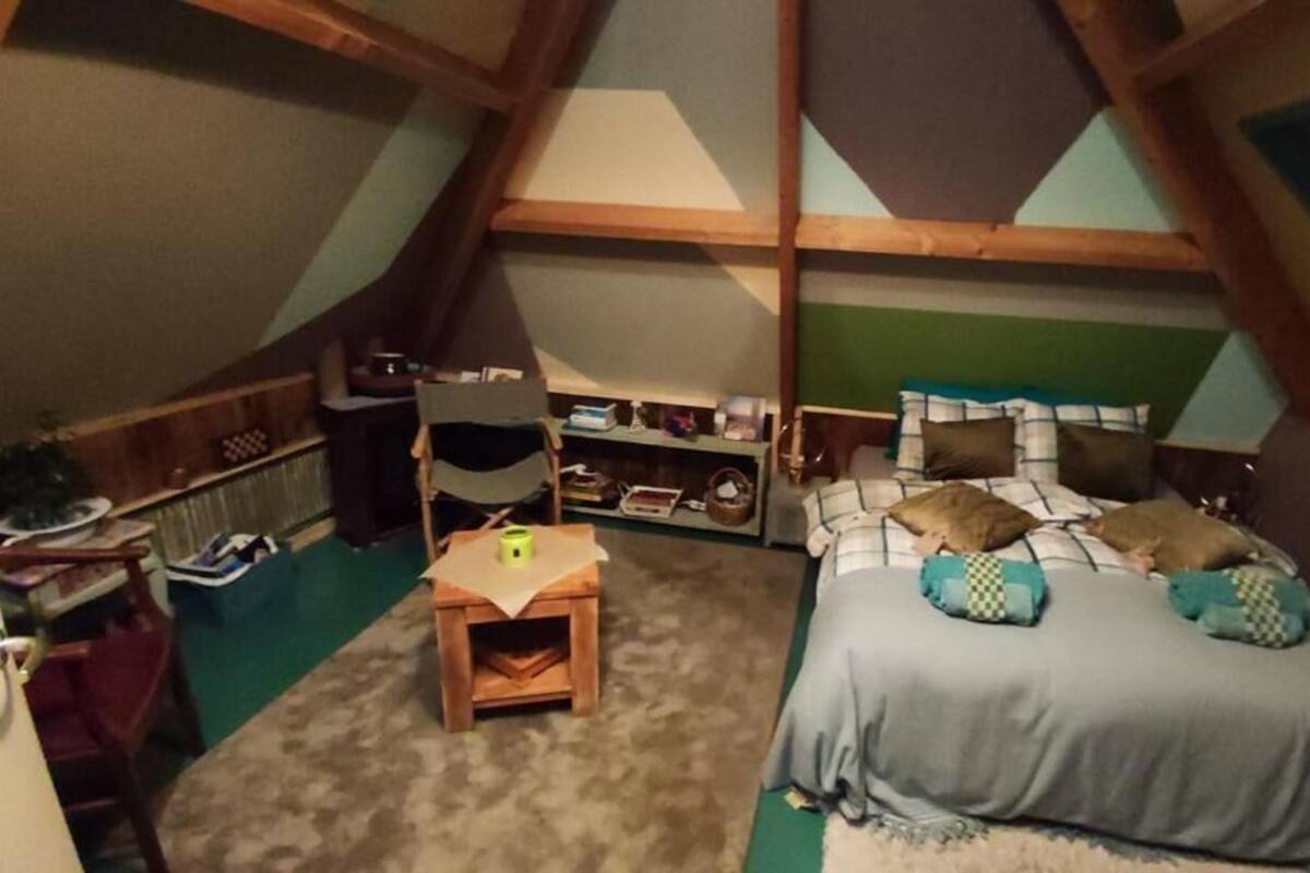 Une chambre mansardée chaleureuse, avec un plafond en pente, un lit avec des oreillers, une petite table et une chaise.