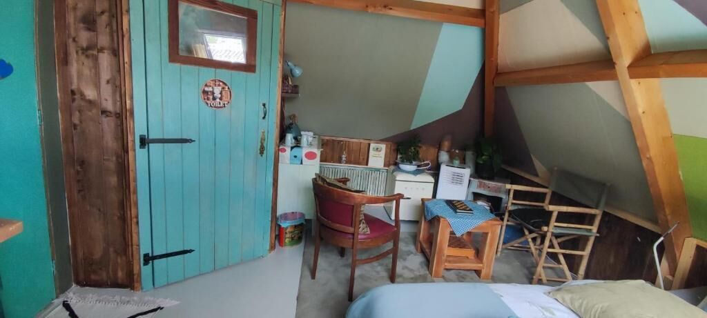 A small, cozy room with a wooden door, a small table with chairs, a radiator, and a window.