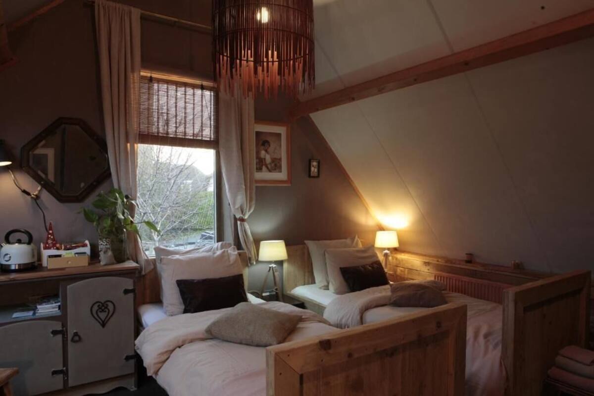 Une chambre à coucher chaleureuse et rustique, avec deux lits en bois, un bureau doté d’un miroir et une fenêtre agrémentée de rideaux.