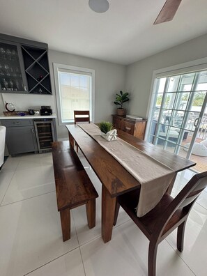 A modern kitchen with a dining area, including a long wooden table, benches, and a view through large sliding glass doors to an outdoor patio. - Canal front 4-bedroom house in Blackwater Sound, Key Largo near Adams Cut (Key Largo)