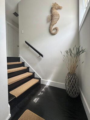 A staircase with black steps and beige carpet runners, a wooden seahorse wall decoration, and a woven vase with tall grasses. - Canal front 4-bedroom house in Blackwater Sound, Key Largo near Adams Cut (Key Largo)