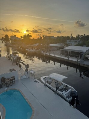 A marina with boats docked, a swimming pool, and a sunset in the background. - Canal front 4-bedroom house in Blackwater Sound, Key Largo near Adams Cut (Key Largo)