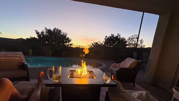 Un patio con una mesa de fuego, sillones de descanso y una piscina al fondo.