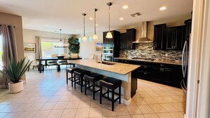 Una cocina moderna con una isla central, iluminación colgante y armarios oscuros.