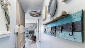 Ein Flur mit einer weißen Tür, einem Wandventilator, einem Fernseher und einem hölzernen Wandregal mit Haken.