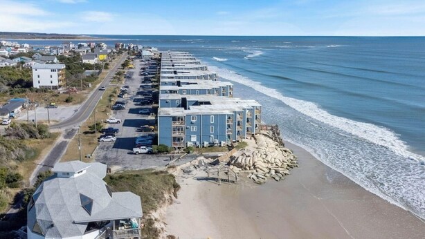 Ein Hotel direkt am Strand mit mehrstöckigen Gebäuden, einem Parkplatz und einem Sandstrand.