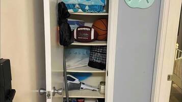 A storage closet with shelves containing folded clothes, a football, a basketball, a broom, and cleaning supplies.