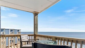 Eine Holzterrasse mit Blick auf das Meer, einem überdachten Bereich und einem kleinen Gebäude im Hintergrund.