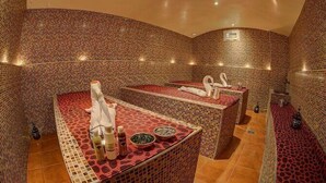 A spa room with two massage tables, a small table with bottles, and a tiled wall. - Sahari Merzouga Camp (Merzouga)