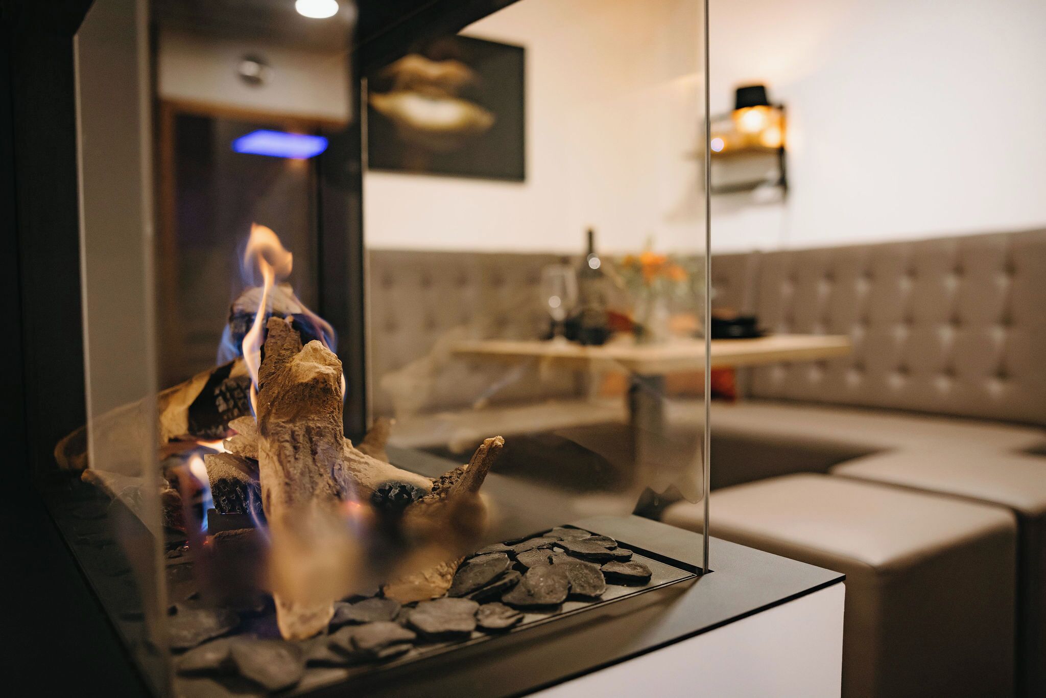 Un interior moderno con chimenea de cristal, zona de estar con cojines y una lámpara fijada a la pared.