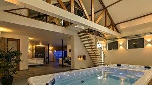Een modern interieur met een bubbelbad, houten balken, een trap en een zithoek.