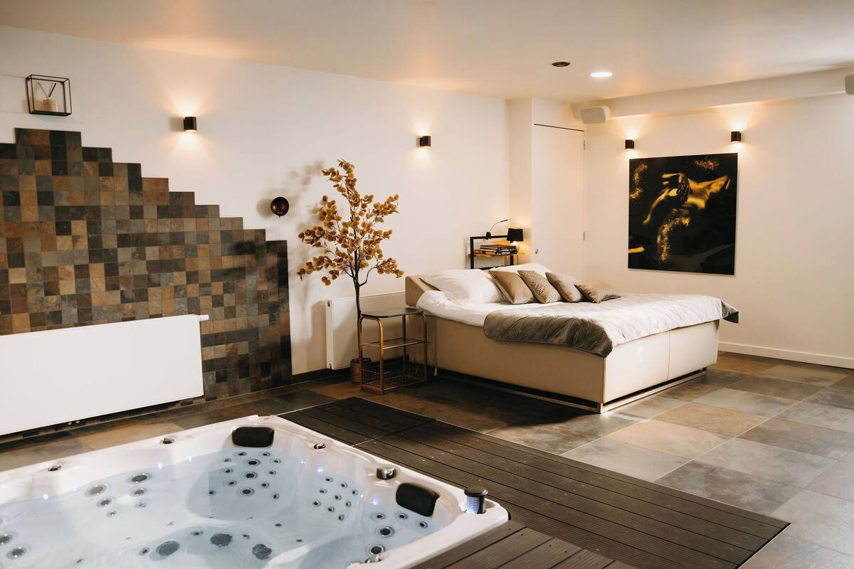 Une chambre moderne avec un grand lit, un jacuzzi et un escalier agrémenté d’un mur en mosaïque.