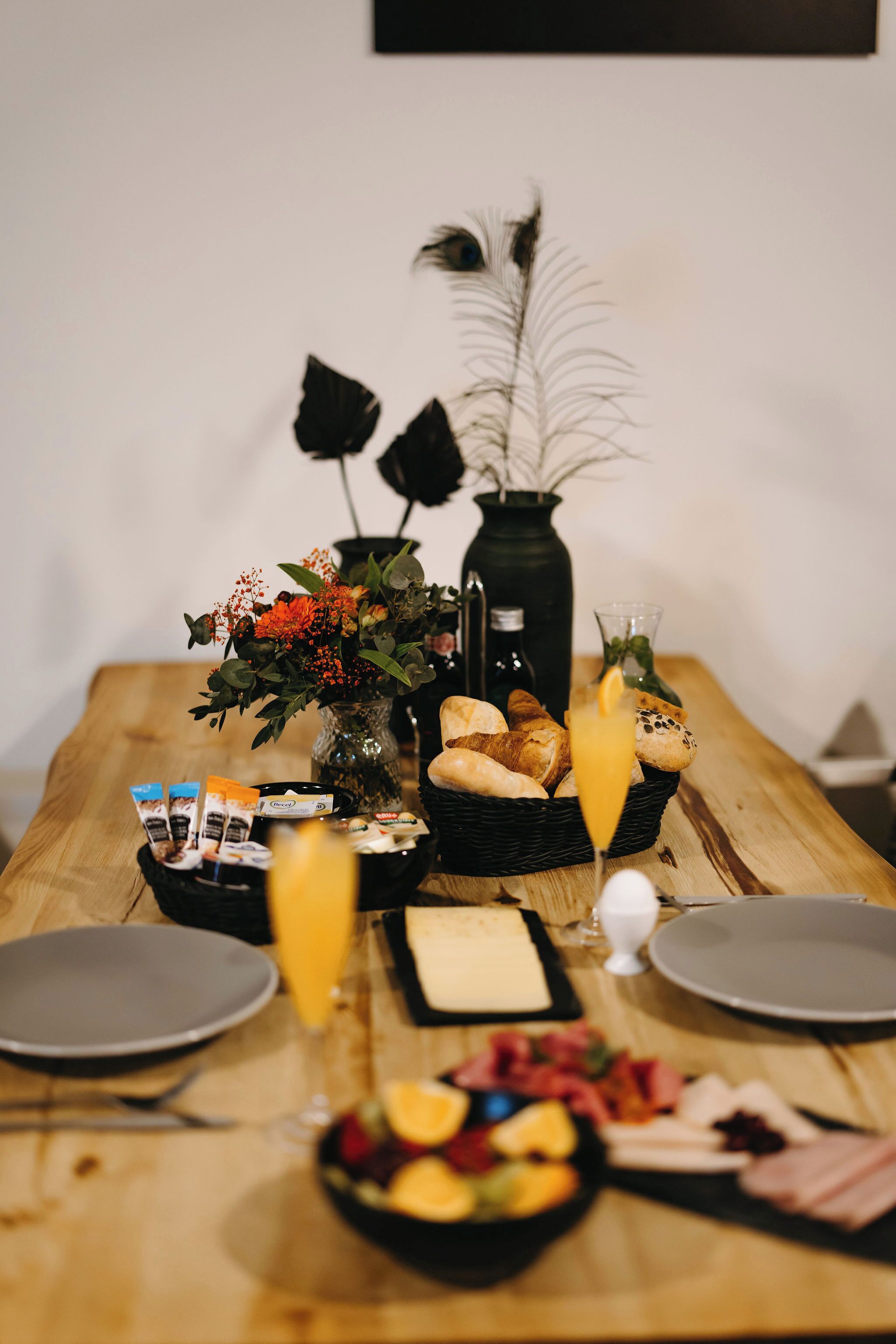 A wooden dining table with a variety of food items, including bread, fruit, and a glass of orange juice.