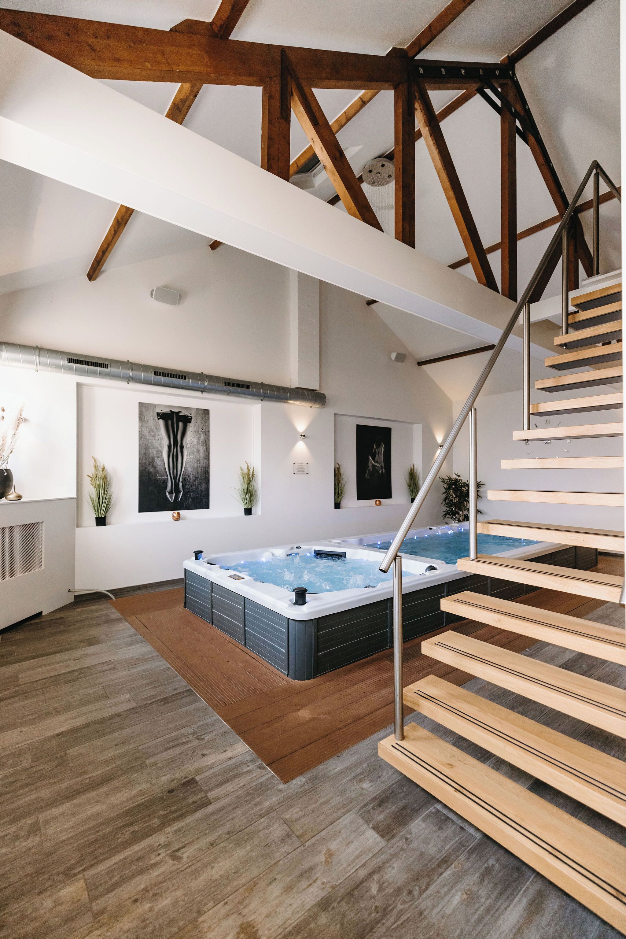 A modern interior with a wooden staircase, a hot tub, and a staircase railing.
