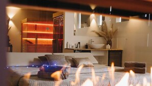 Een modern interieur met een bed, nachtkastje en een zichtbare badkamer met wastafel en spiegel.