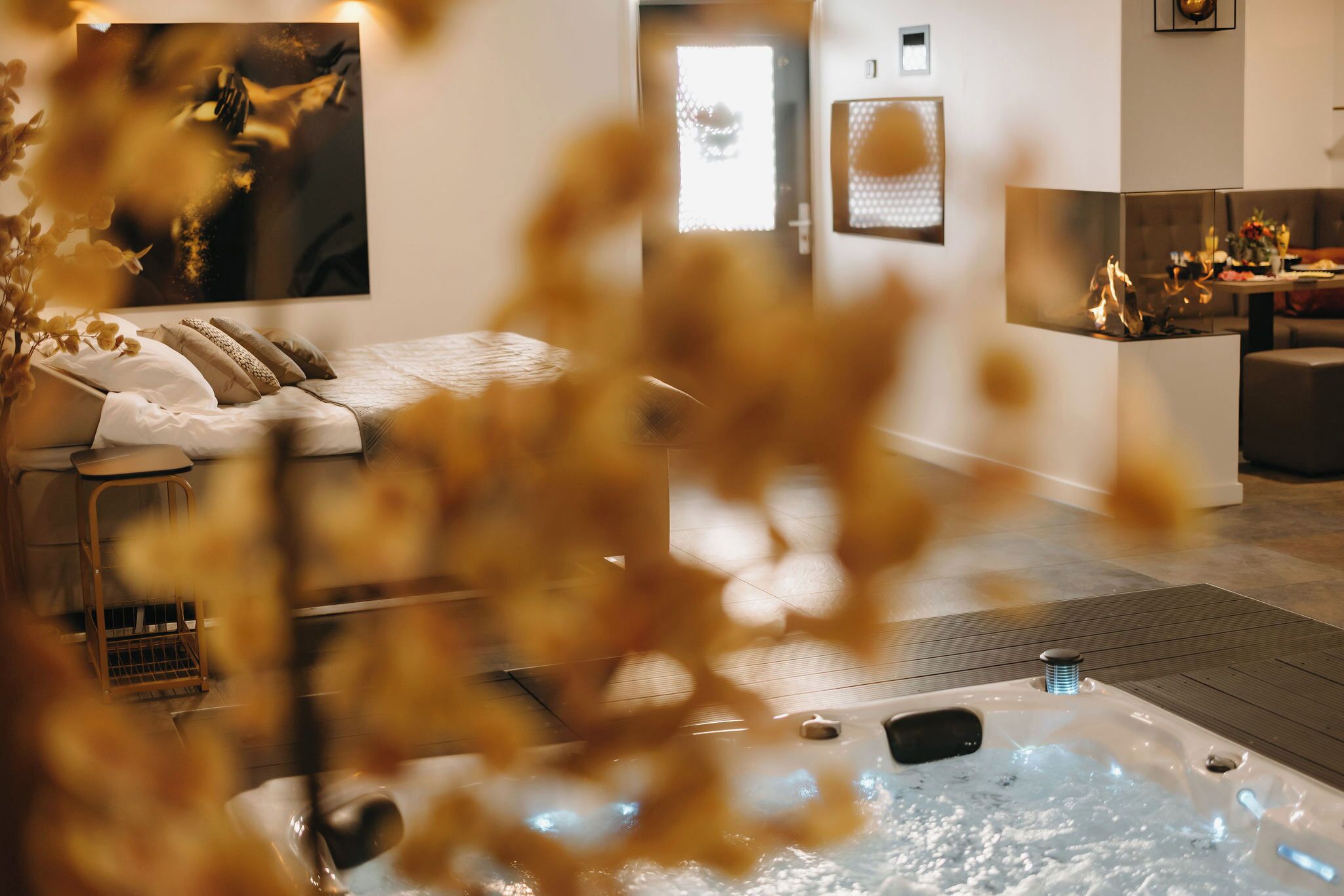 Ein modernes Hotelzimmer mit Bett, einer Sitzecke mit Tisch, einem Kamin und einem großen Fenster.