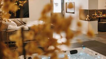 Ein modernes Hotelzimmer mit Bett, einer Sitzecke mit Tisch, einem Kamin und einem großen Fenster.