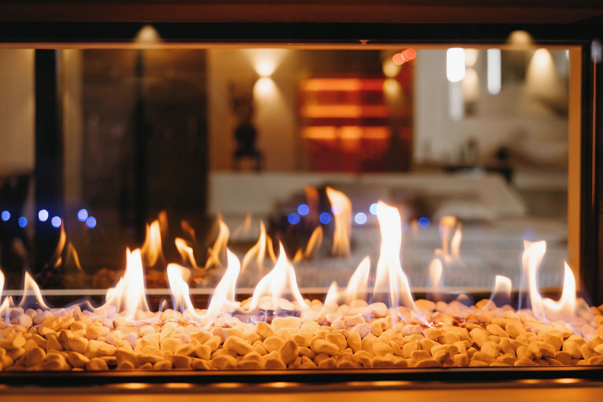 A fireplace with burning logs and a view of a room with a bed and a nightstand.