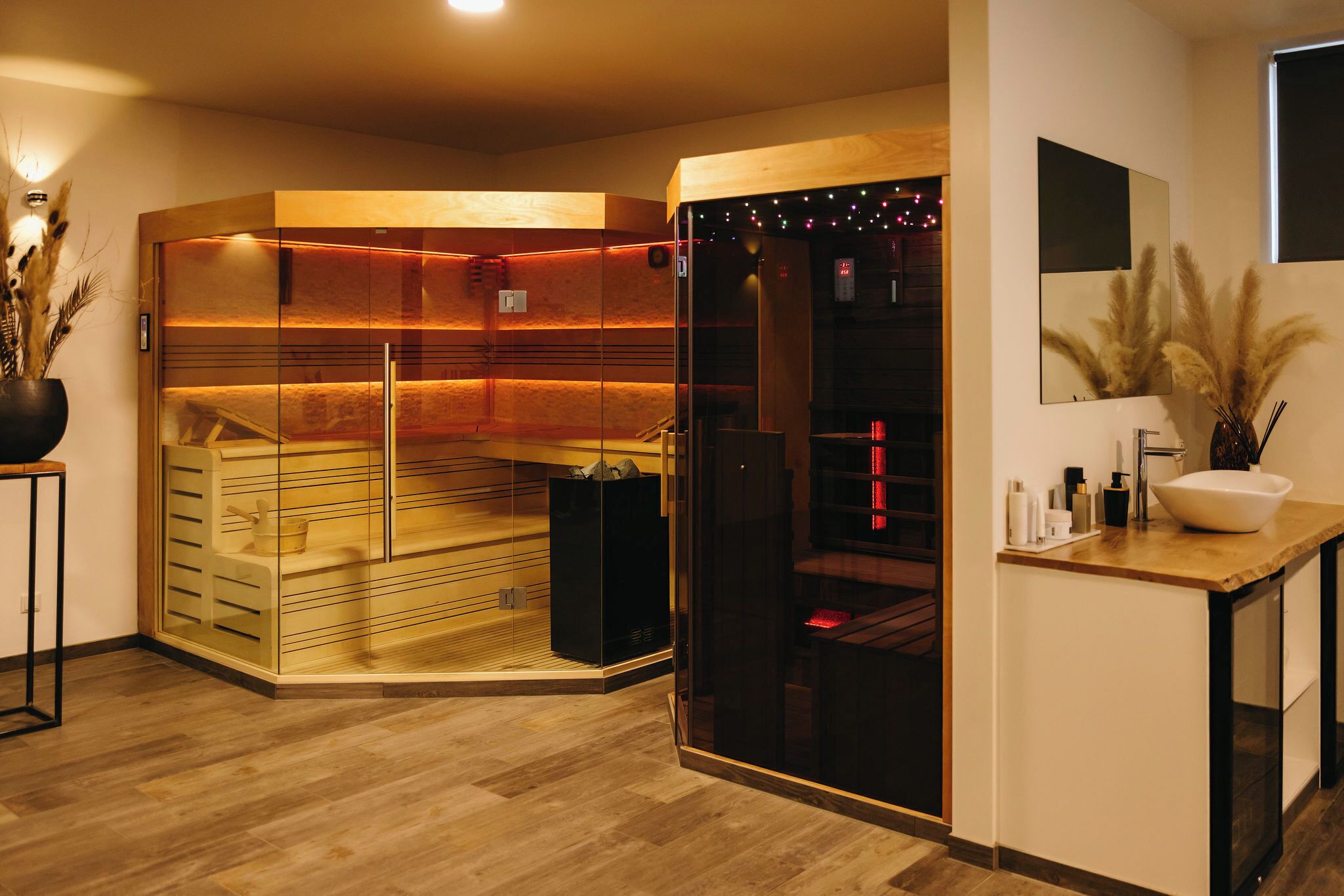 A modern spa room with a wooden sauna, a glass-enclosed shower area, and a wooden vanity with a sink and toiletries.
