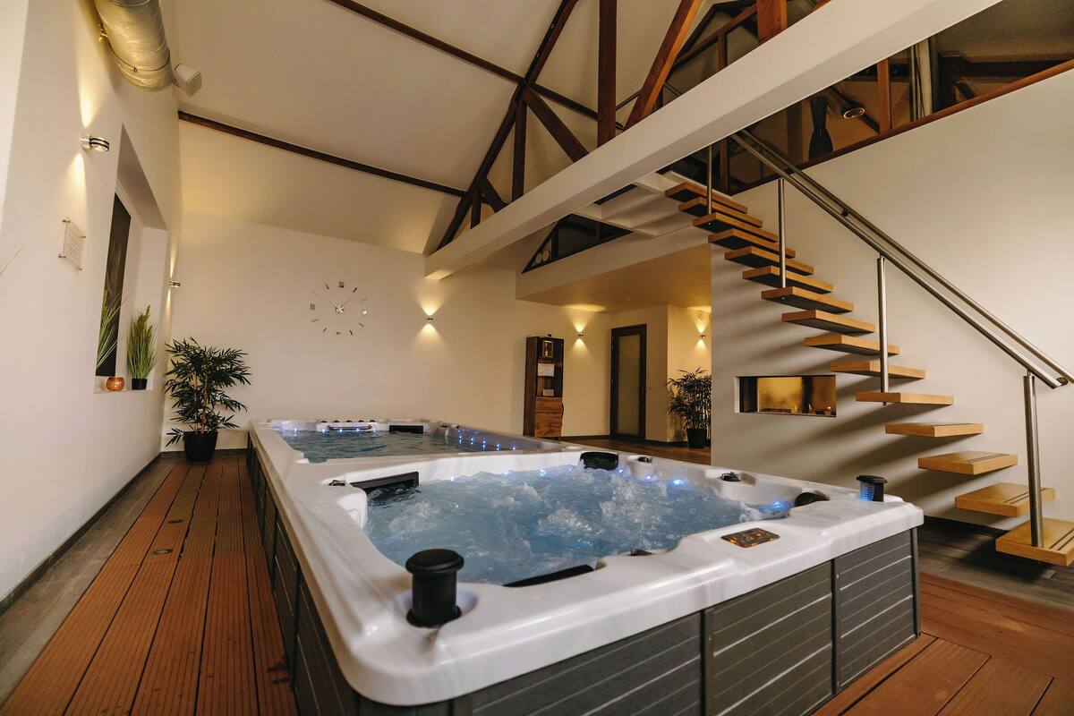 Un espace spa moderne doté d’un jacuzzi, de revêtements de sol en bois et d’un escalier.
