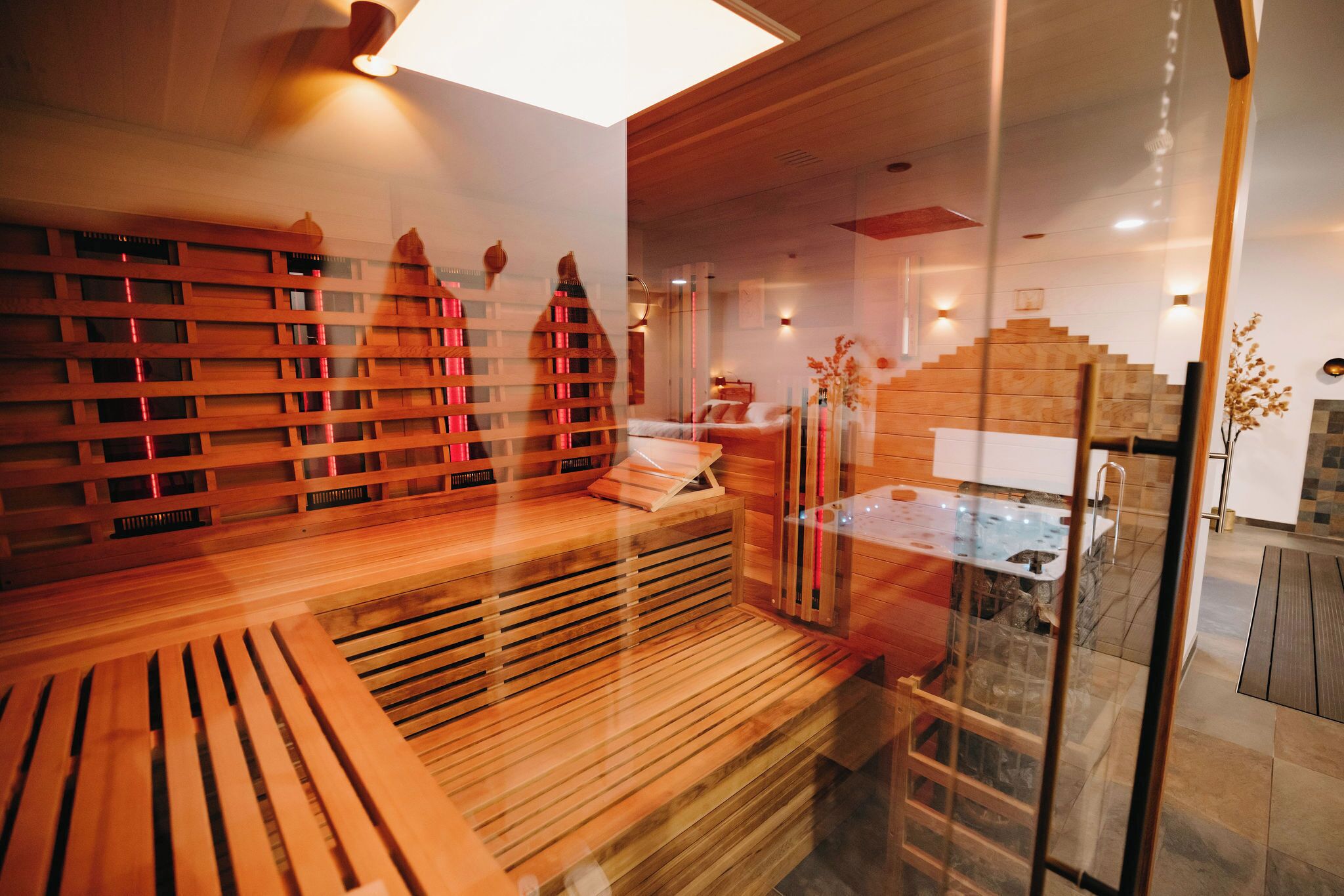 Ein moderner Wellnessbereich mit Holzbänken, einer in Glas eingefassten Whirlwanne und einer Holztreppe.