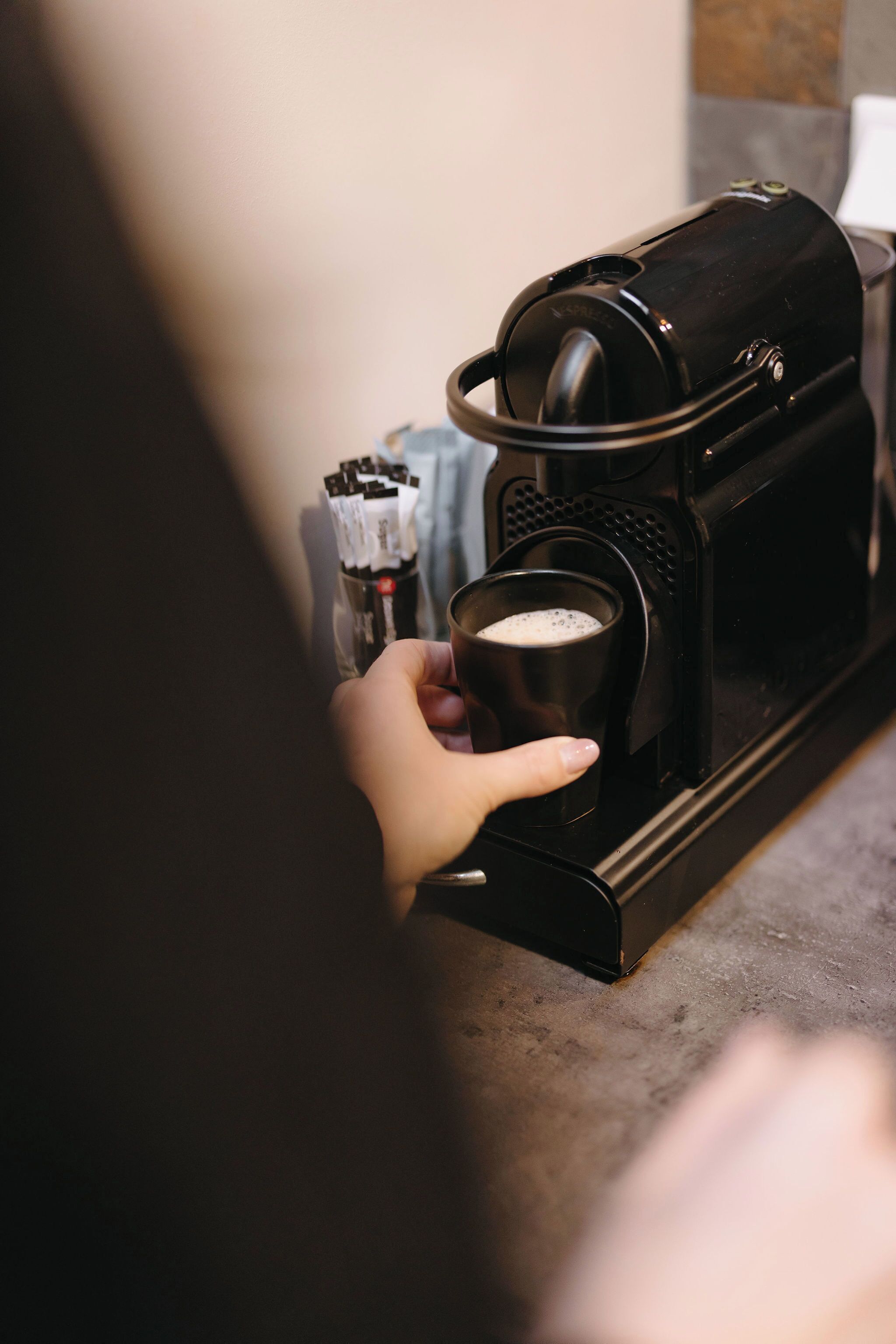 A hand holding a cup near a coffee machine.
