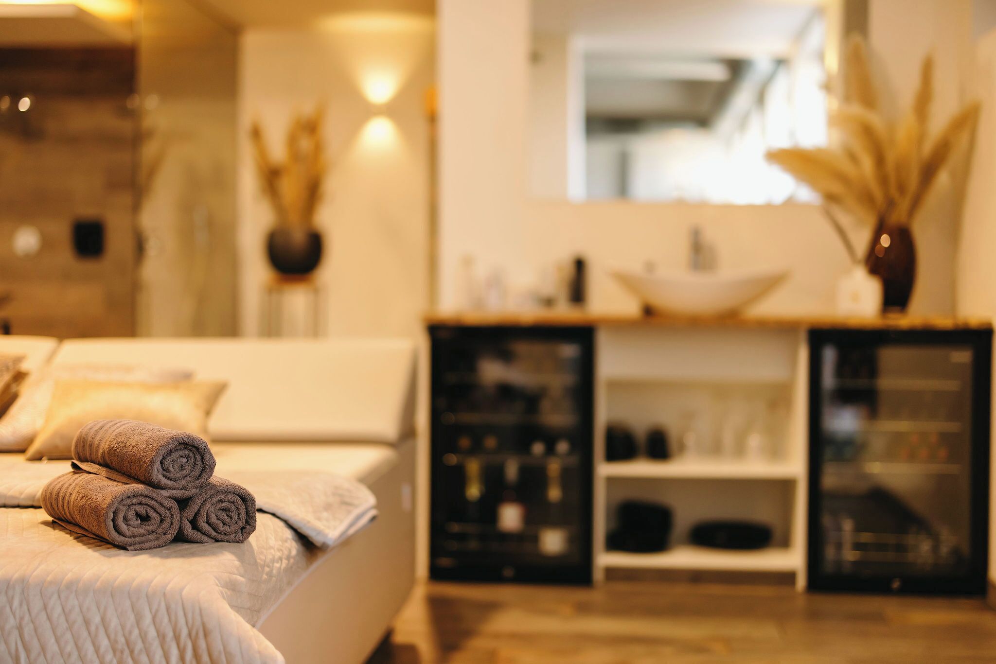 Een keurig opgemaakt bed met opgerolde handdoeken, een grote spiegel en een houten kast met planken.