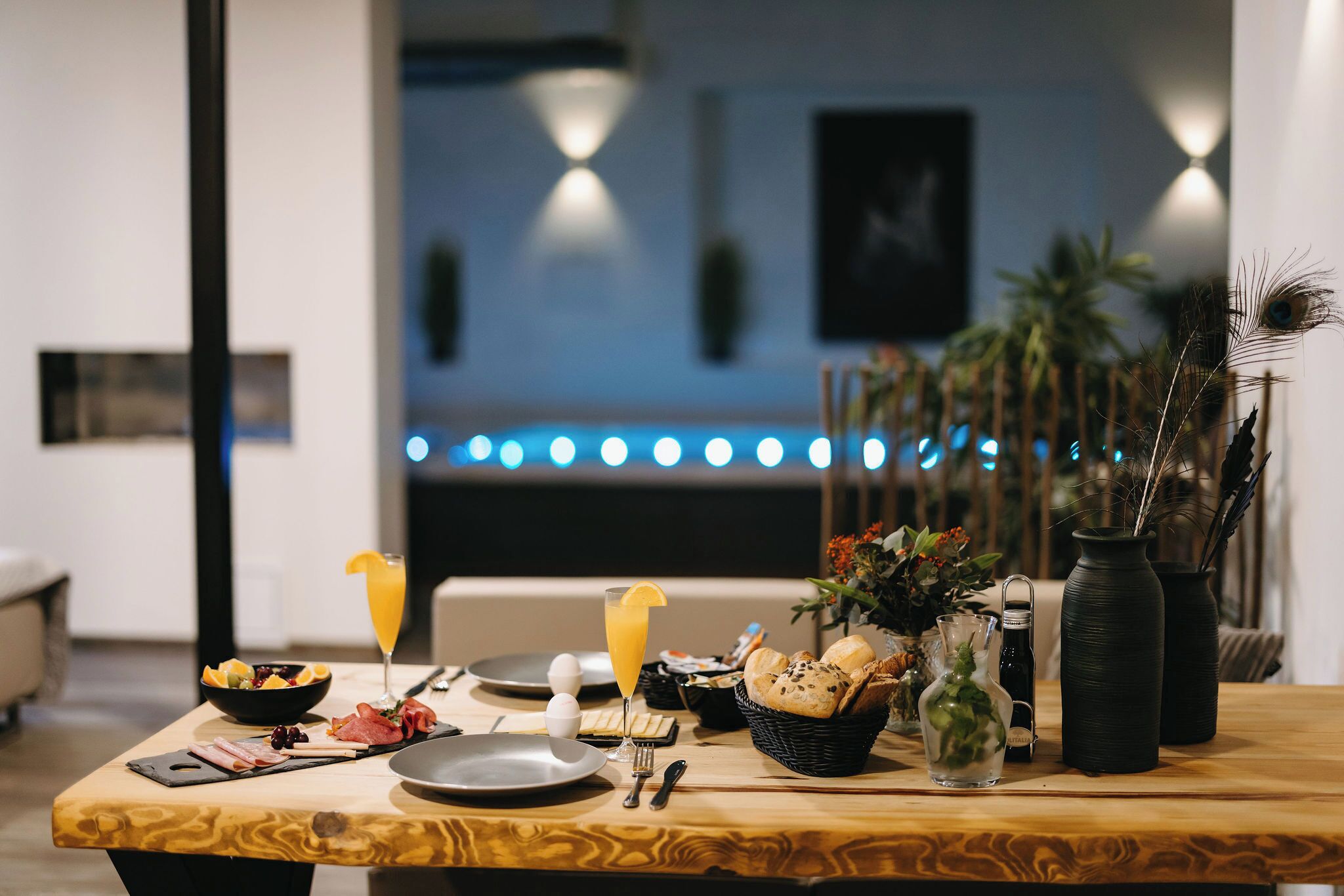 Une table de petit-déjeuner avec des assiettes, des couverts, un verre de jus d’orange et un panier de pain.