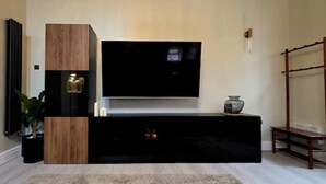Moderni olohuone, jossa on seinälle asennettu taulutelevisio, joka on kiinnitetty puiseen kaappiin, pieni pöytä maljakolla ja puinen tuoli.