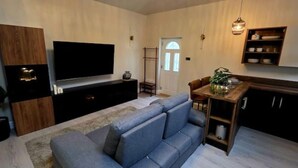 Un salon comprenant un canapé, un téléviseur à écran plat, un meuble en bois et un coin repas avec une table et des chaises.