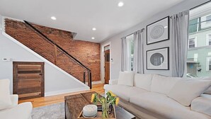Ein modernes Wohnzimmer mit einem weißen Sofa, einem Couchtisch mit Tablett, einer Ziegelwand und einer Treppe.
