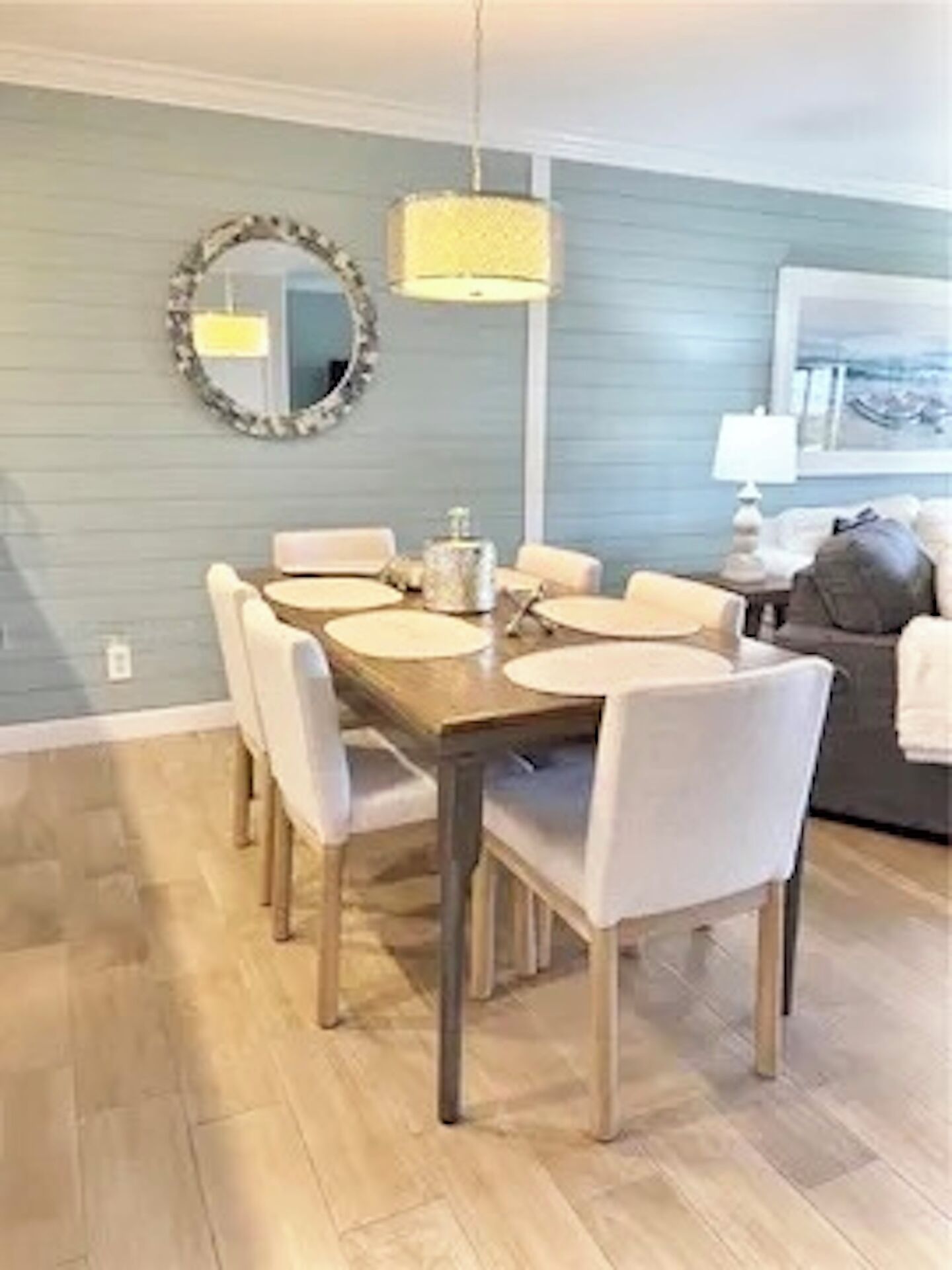 A dining area with a round table, chairs, a hanging light fixture, and a mirror on the wall.