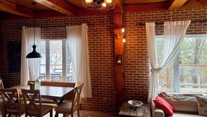 A cozy room with a brick wall, wooden ceiling, a dining table with chairs, a sofa, and a window with curtains. - The Hidden Gem (Gracefield)