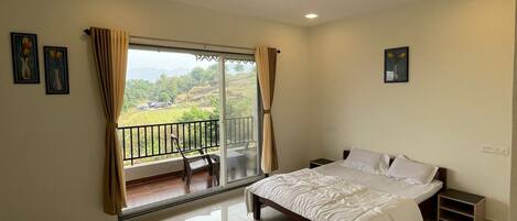 A bedroom with a bed, a ceiling fan, a balcony with a view of greenery, and a window with curtains.