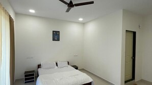 Una camera da letto con un letto, una ventola a soffitto, una porta e un piccolo quadro appeso al muro.