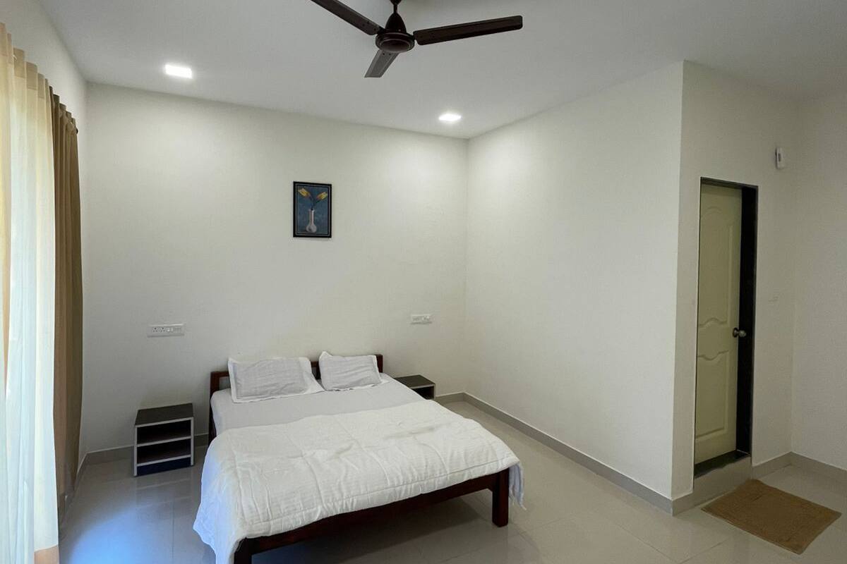 A bedroom with a bed, a ceiling fan, a door, and a small picture on the wall.