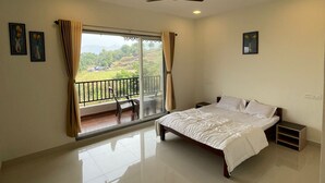 Camera da letto con un letto, una ventola a soffitto, un balcone con una sedia e vista sul verde.