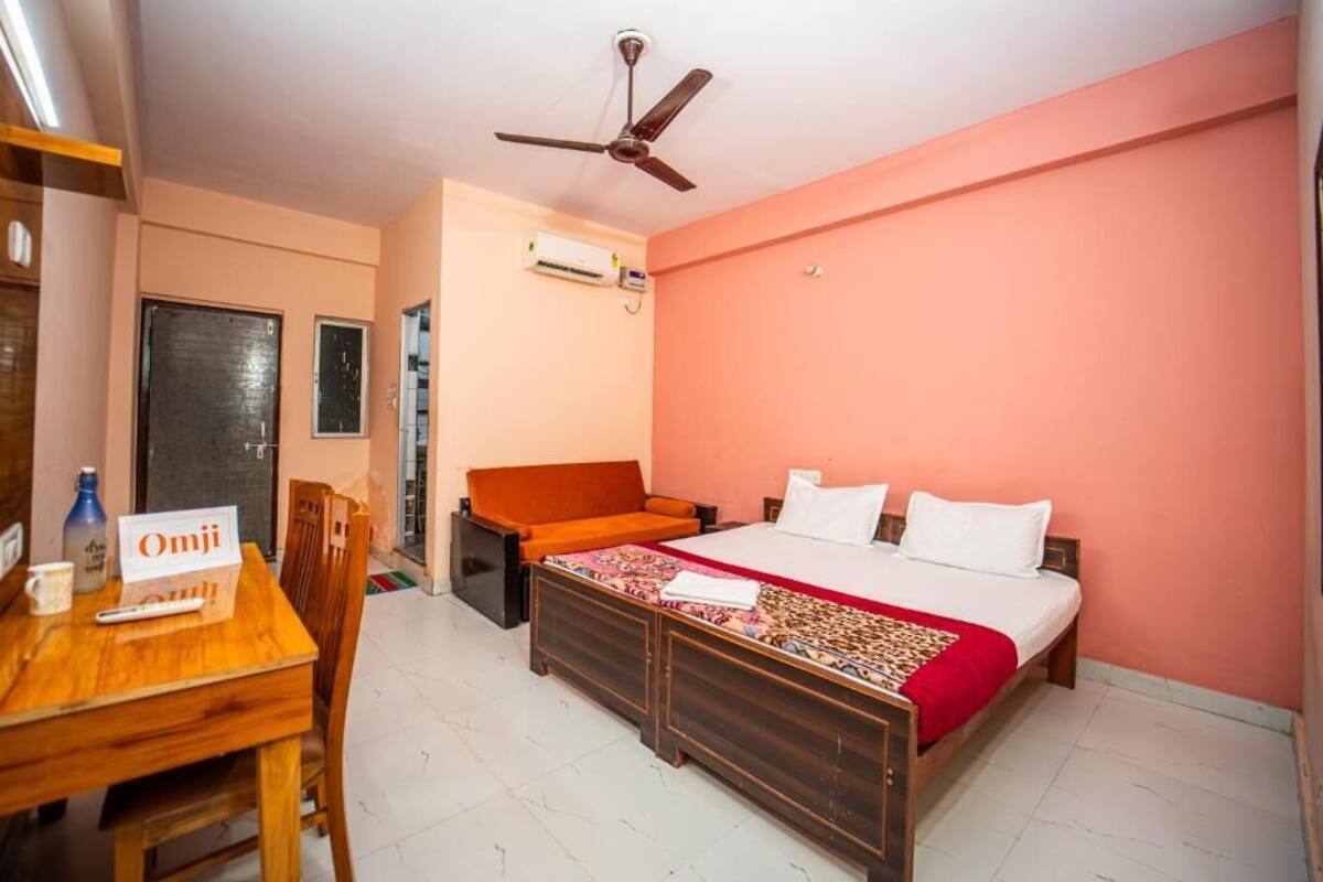 A bedroom with a bed, a desk with a chair, a sofa, a ceiling fan, and an air conditioning unit.