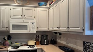 Une cuisine avec des armoires blanches, un four à micro-ondes, une cuisinière et un panneau affiché sur le mur.