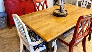 Un coin repas avec une table en bois, des chaises blanches, un buffet rouge et un porte-bouteilles fixé au mur.