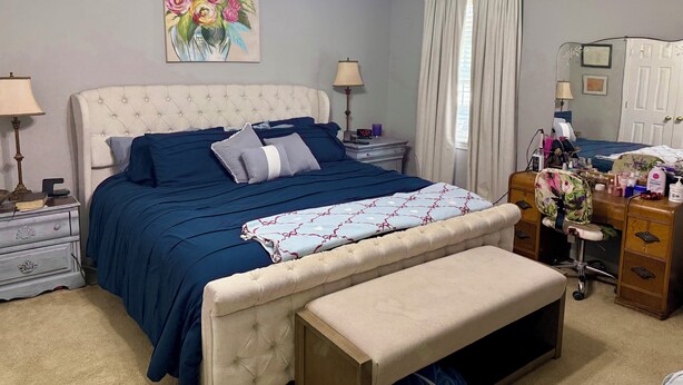 Une chambre à coucher comprenant un lit, des tables de chevet, une commode, une coiffeuse, un fer à repasser et un ventilateur de plafond.
